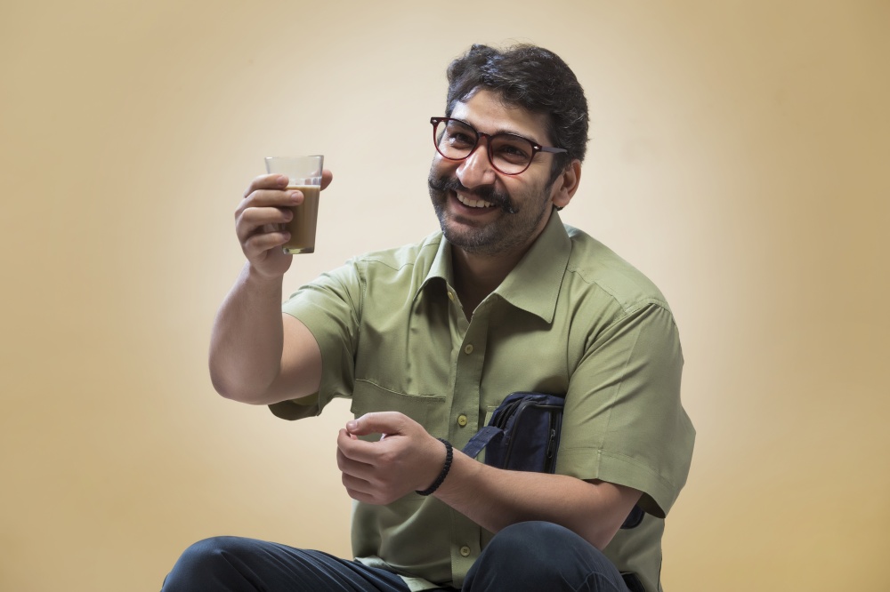 Smiling man wearing eyeglasses holding a small pouch and looking at a glass of tea in his hand.