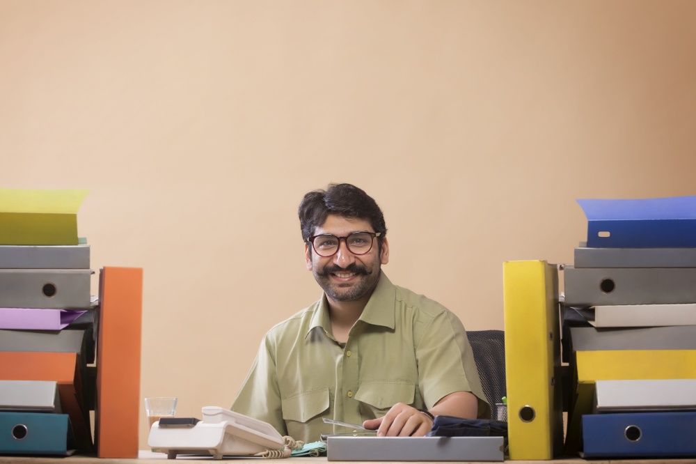 Smiling businessman looking at files sitting at his office desk with a glass of tea in his hand.