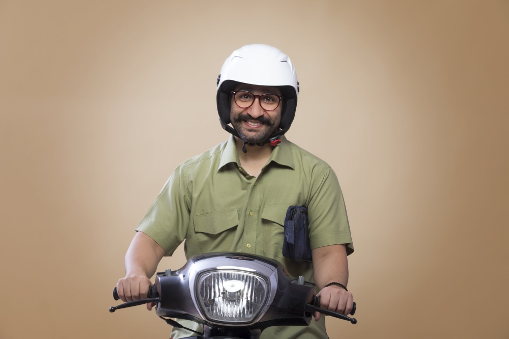 Smiling man with a small bag in his arms riding scooter wearing a helmet.