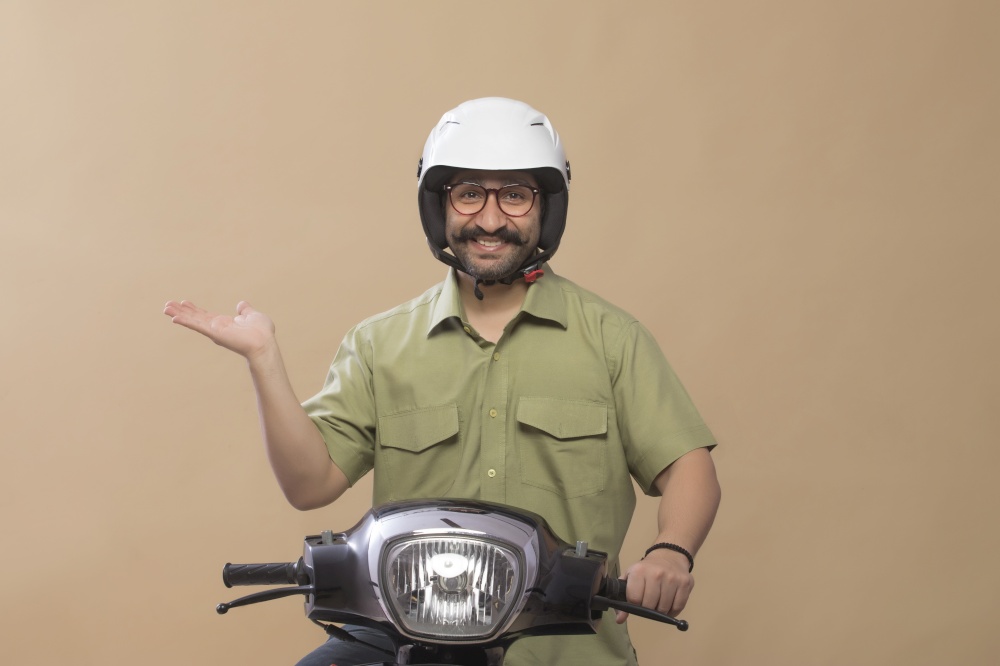 Smiling man wearing helmet sitting on a scooter and showing palm.