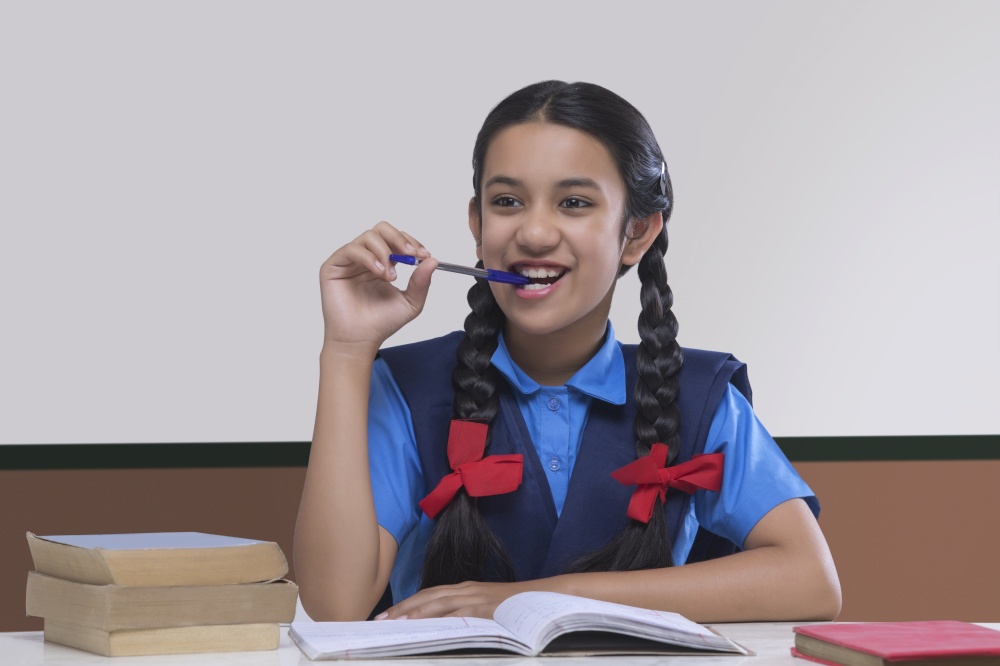 Smiling school girl holding pen in mouth