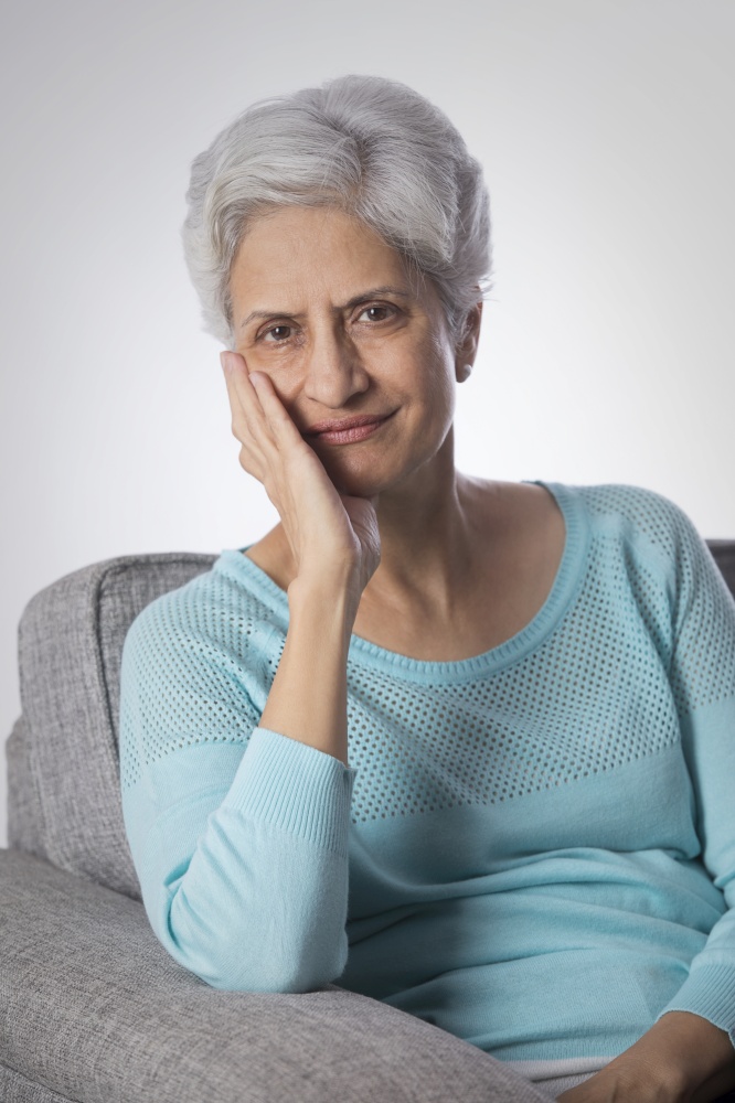 Portrait of senior woman thinking sitting on sofa with hand on chin