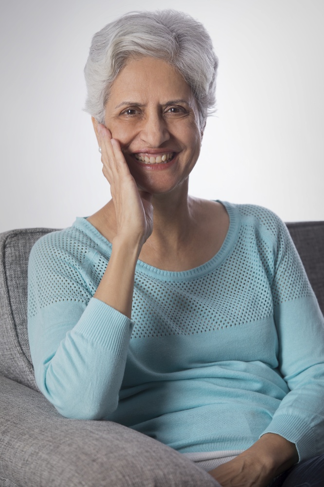 Portrait of senior woman smiling sitting on sofa with hand on chin