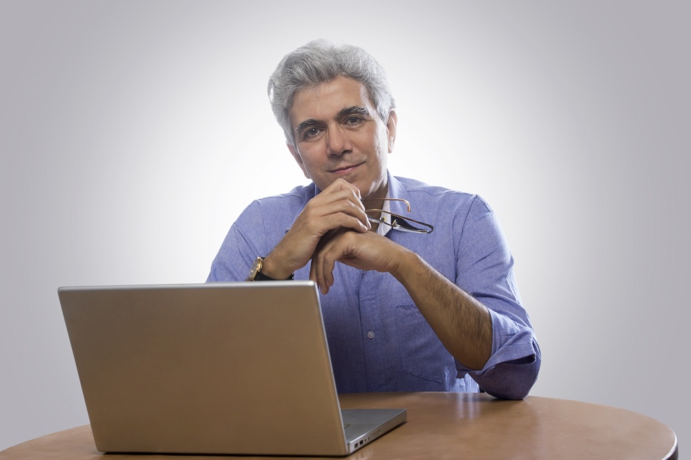 Portrait of senior man sitting at table with laptop