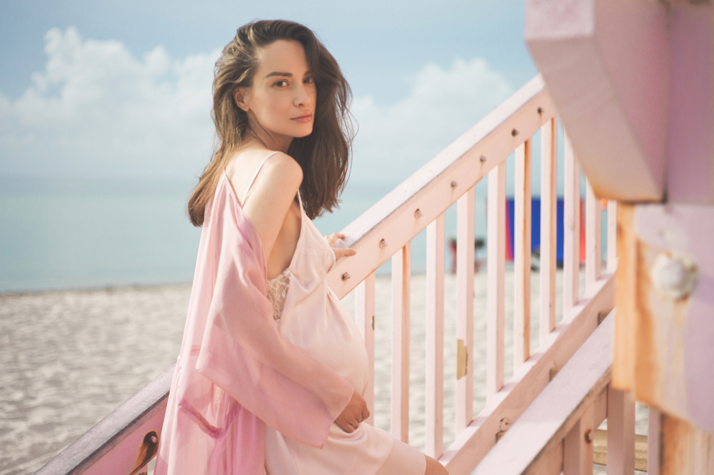 Outdoor atmospheric lifestyle portrait of beautiful pregnant woman in pink dress on pink lifeguard tower. Beautiful morning. Sunrise on the beach. Beauty and fashion. Pink aesthetic