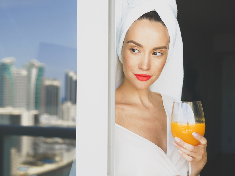 Young beautiful  woman on balcony with glass of orange juice. Beautiful morning. Fashion and beauty