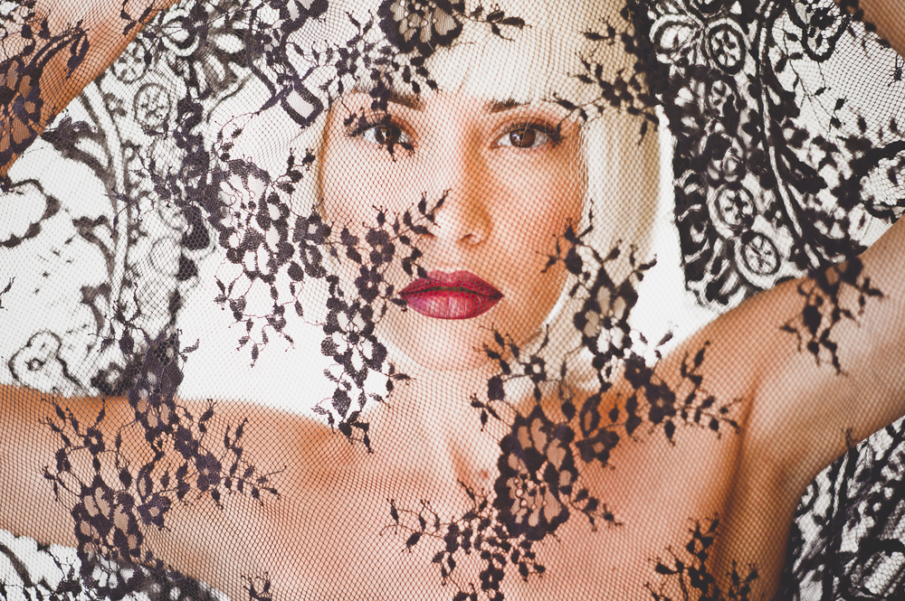 Fashion portrait of beautiful blond woman with lace in front of her face