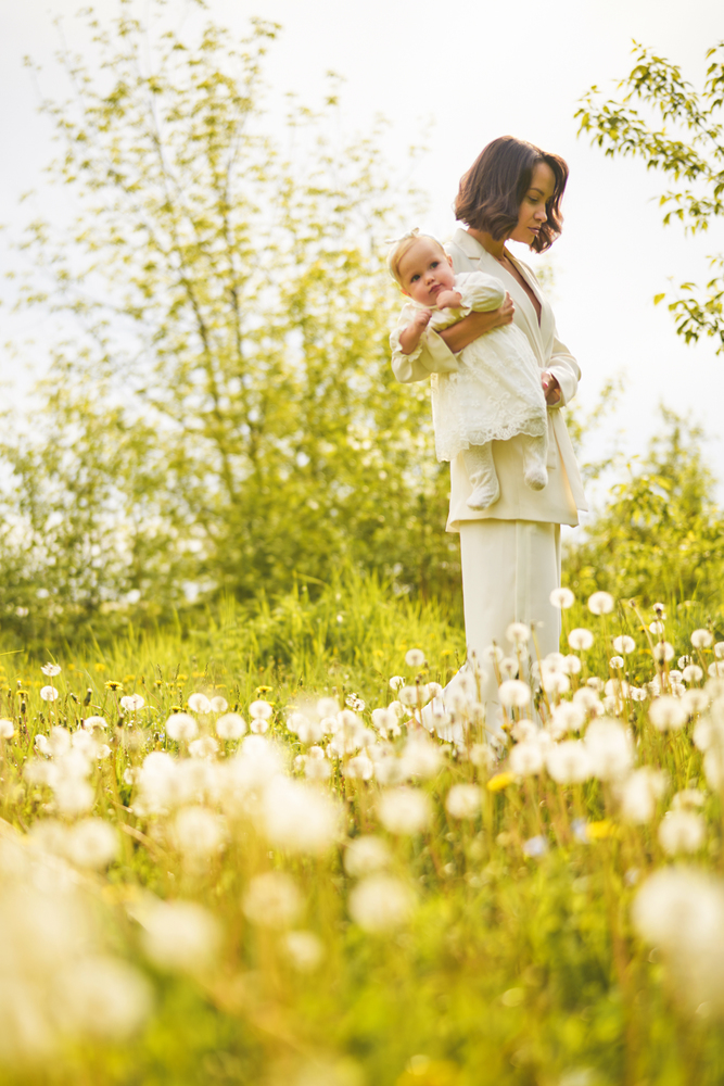 Outdoor fashion portrait of young beautiful mother and little cute daughter on a meadow with dandelions. Spring image
