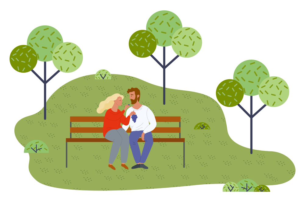 Young couple relaxing at bench in park, girl holding grape, feeding boyfriend with berries. Happy in love people spending time together outdoors at nature. In love man and woman have light picnic. Young couple relaxing at bench in park, girl holding grape, feeding boyfriend with berries