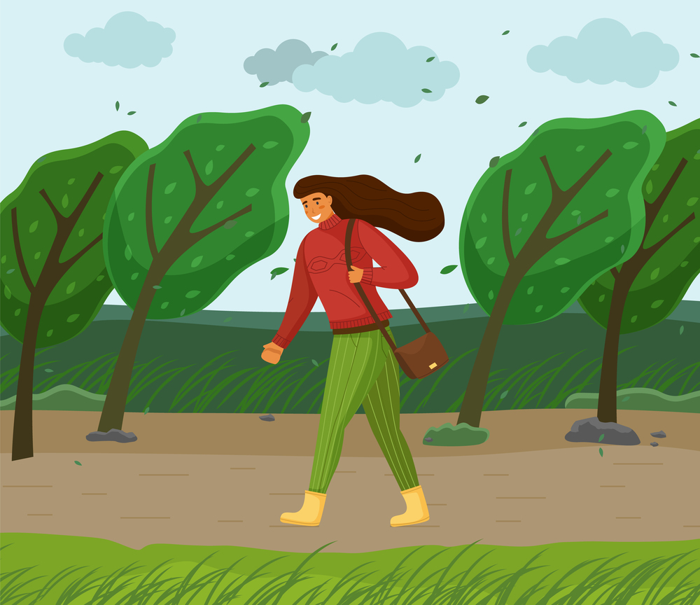Windy weather, woman walking in park through strong wind, green trees bend, leaves flying in air, young girl with brown long hair, red warm sweater, green striped pants, bag on shoulder, boots. Windy weather, woman walking in park through strong wind, green trees bend, leaves flying in air