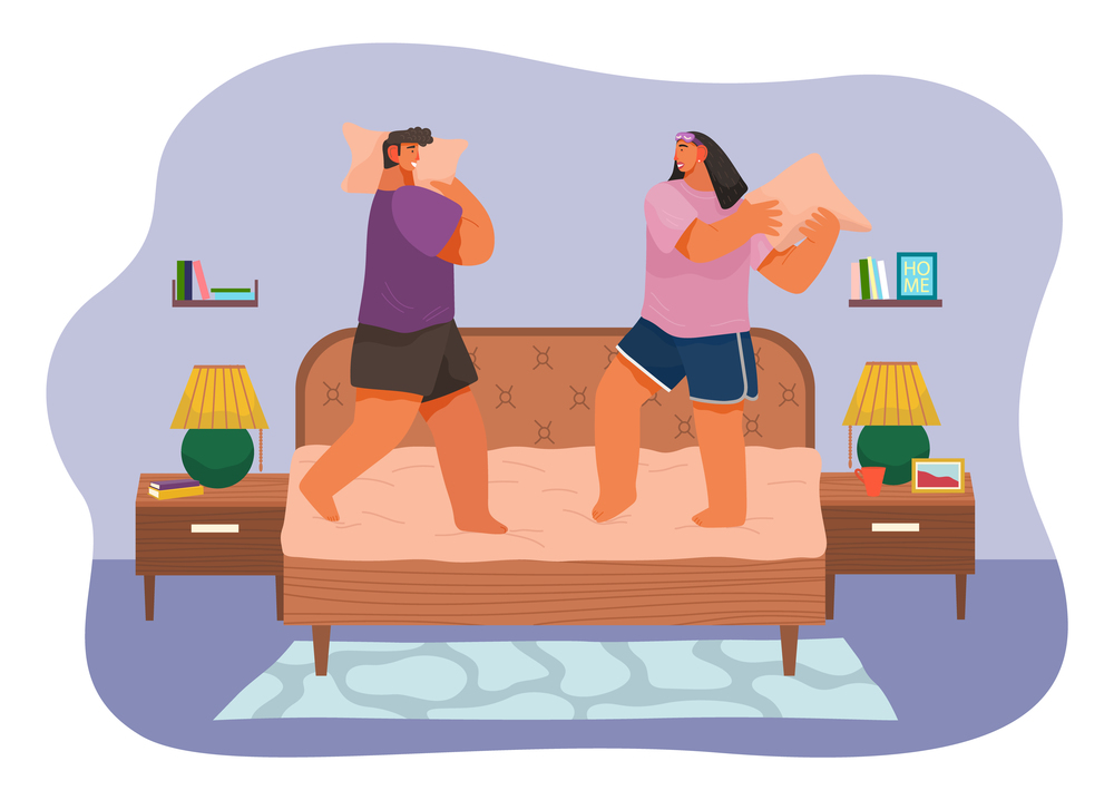 Couple fighting pillows, playing childhood game, have fun together at home. Man and woman rejoice standing at bed. Two adult friends playing. Romance fighting of pillows of girlfriend and boyfriend. Couple fighting have fun rejoice fighting pillows standing at bed, happy woman and man play kid game