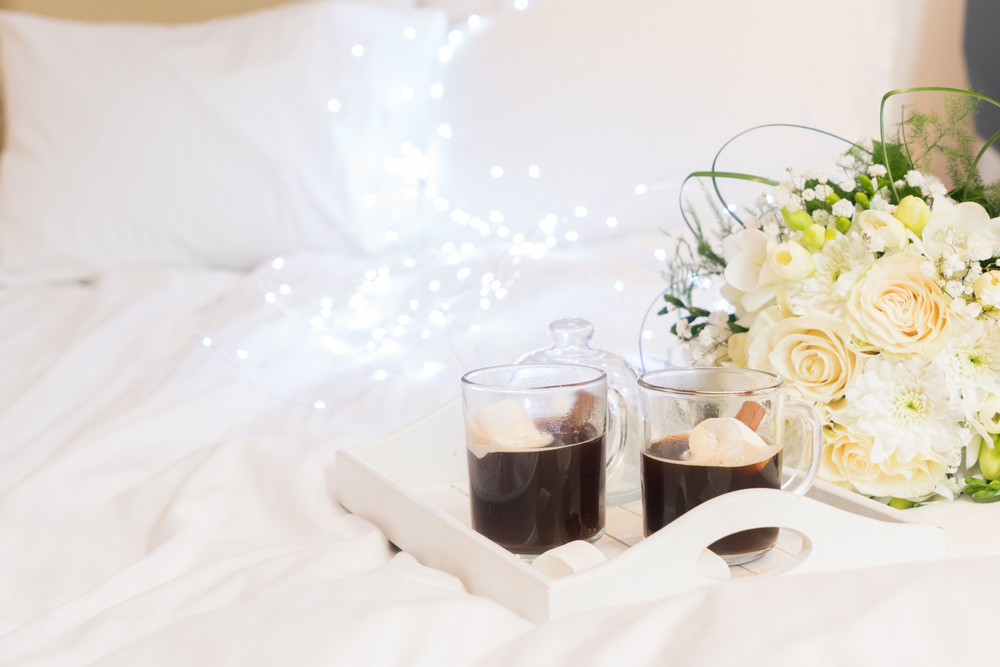 Breakfast in bed - tray with warm coffee drink, flowers and marshmallows, cozy hygge home style. Breakfast in bed
