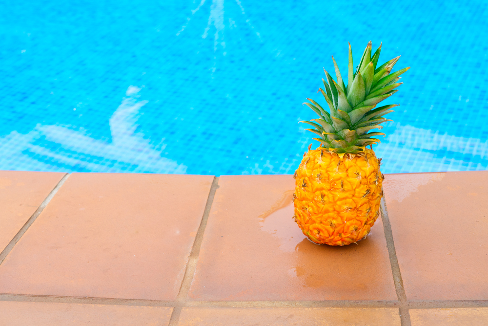 Raw whole yellow pineapple and tiled pool with blue water. Pineapple and pool