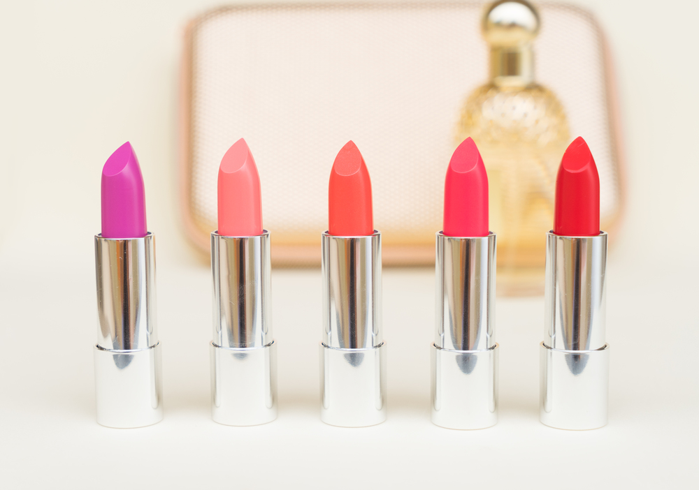 Collection of puple, pink and red shiny lipsticks in front of gold woman pursue. Collection of lipsticks