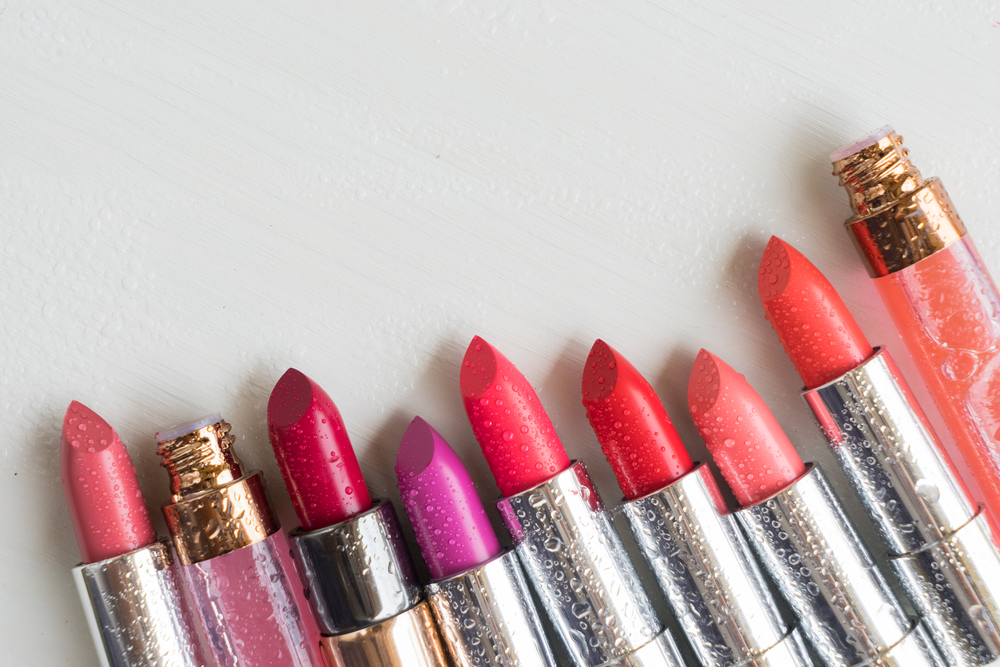 Row of lipsticks in water drops with copy space on beige desktop. Collection of lipsticks