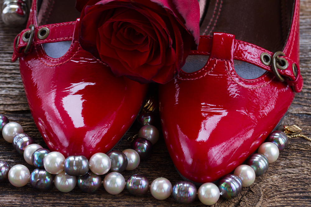 pair of red shoes with rose flower and pearl jewellery  close up . red shoes with rose flower