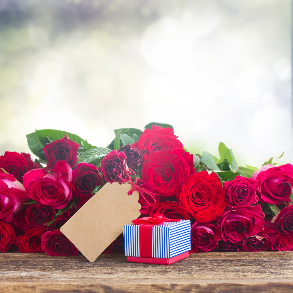 red and pink  roses  with gift box and paper note on wooden table, copy space on gray bokeh backdrop. Border of red roses
