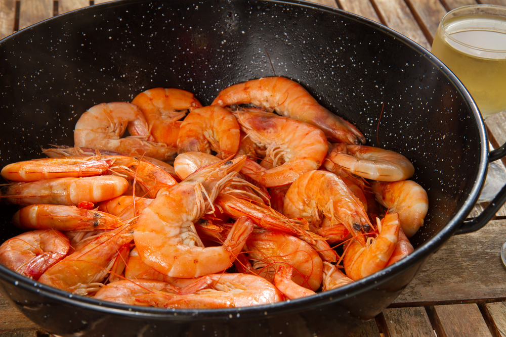black pan with  red cooked  prawns close up  on wooden table. pan with king  prawns