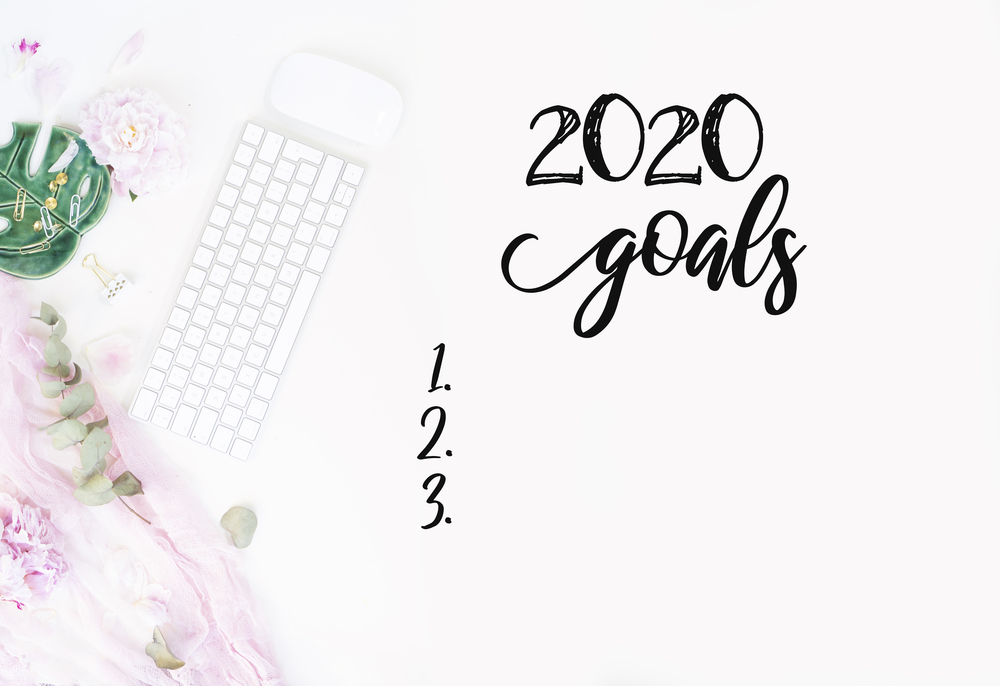 Top view 2020 goals list with modern silver keyboard with female accessories and peony flowers, copy space on white background. Top view home office workspace