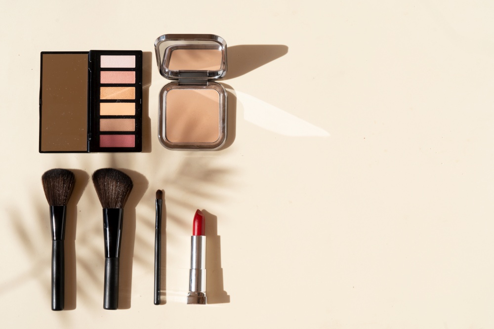 Minimal modern cosmetic scene with make up brushes, eye shadows palette, lipstick, powder and shadow overlay, top view with copy space. make up brushes