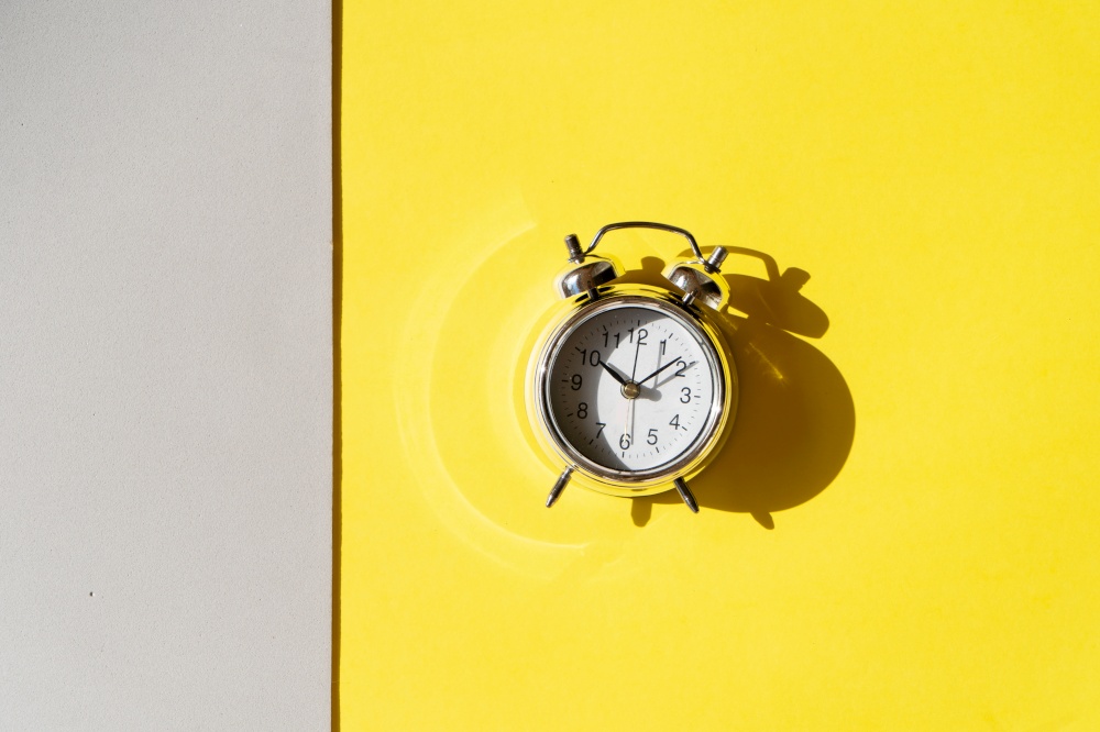 gray alarm clock on illuminating yellow and ulimate gray background, top view. gray alarm clock