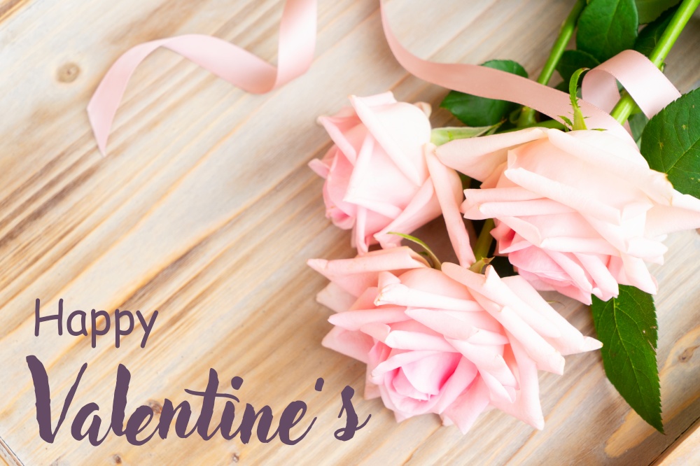 fresh blooming pink roses laying on wooden table, with happy valentines day greeting. pink roses on table