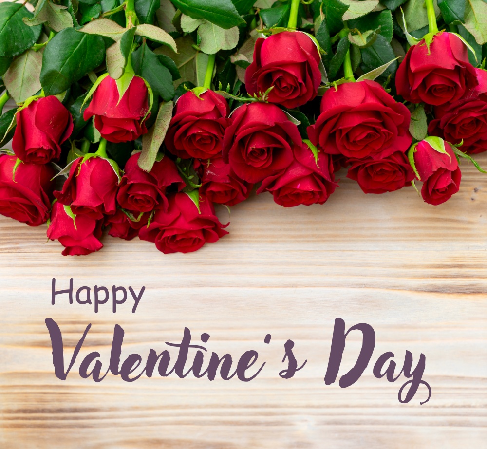 dark red fresh roses laying on wooden table, with happy valentine&rsquo;s day greeting. dark red roses on table