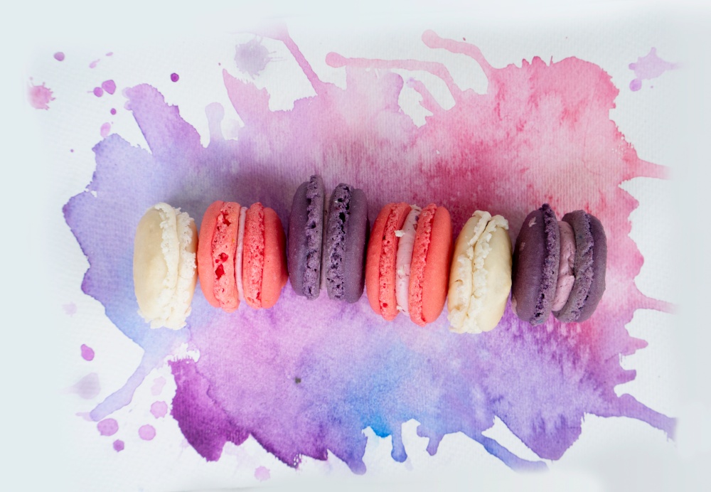 row of french cookies macaroons on watercolor background, top view. french cookies macaroons