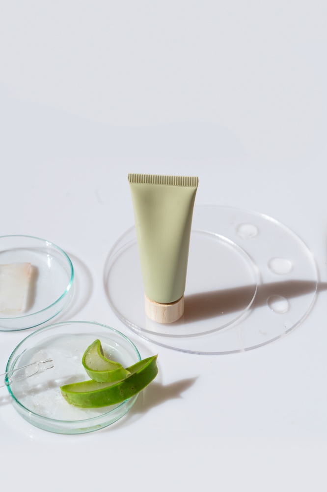 Glass petri dish with transparent pure serum for skin care with cosmetic tube and aloe vera pieces on white background, top view. Concept laboratory tests and research, making and testing cosmetic. Glass petri dish with transparent pure serum for skin care
