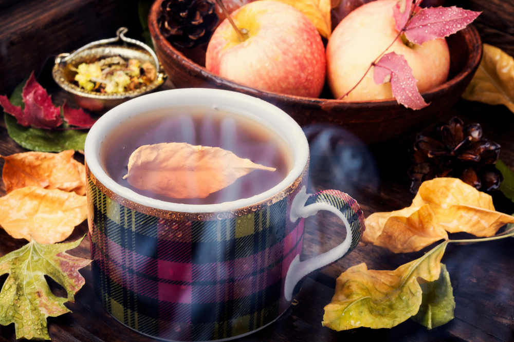 Teacup on an autumn background of fallen leaves and apples .Autumn postcard. Autumn still life with tea cups
