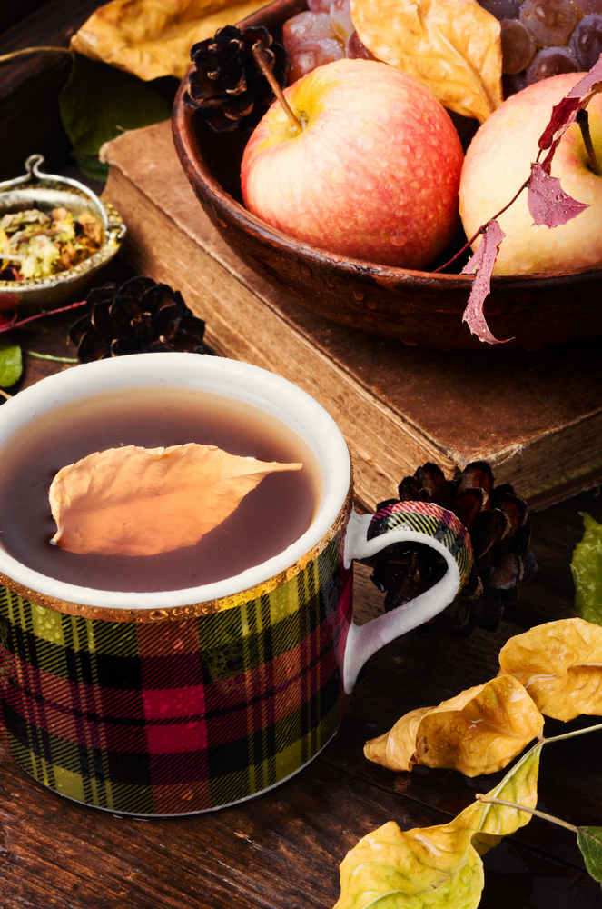 Teacup on an autumn background of fallen leaves and apples .Autumn postcard. Autumn still life with tea cups
