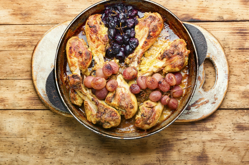 Baked chicken legs with grapes on rustic wooden table. Baked chicken drumsticks