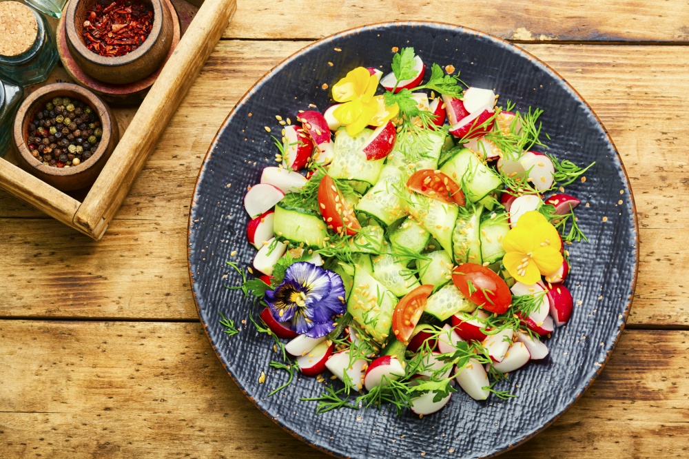 Cucumber,tomato,radish and greens salad decorated with edible flowers.Spring vitamin salad. Green vegan salad