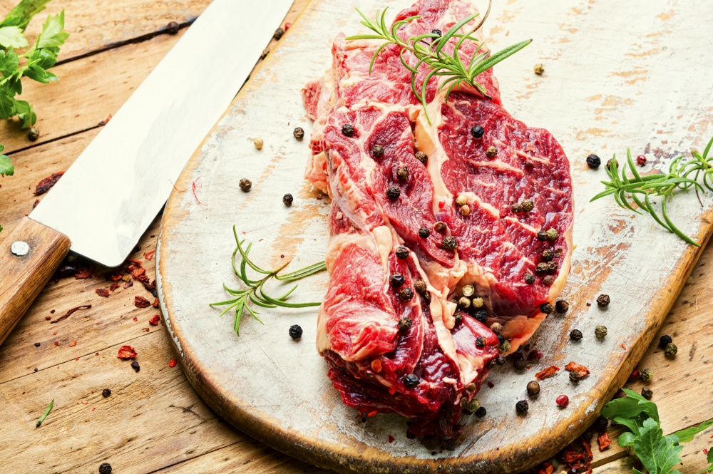 Raw beef meat with rosemary and spices on wooden cutting board. Raw beef meat