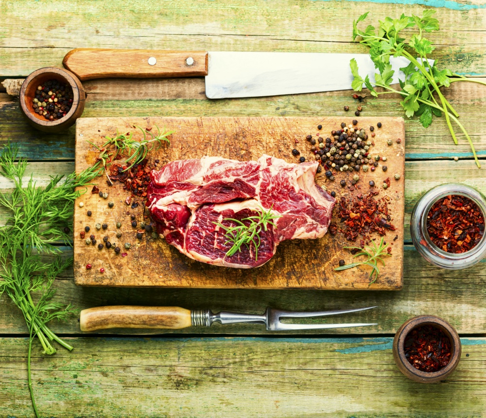 Raw beef meat with rosemary and spices.Uncooked beef steak. Raw meat wooden cutting board