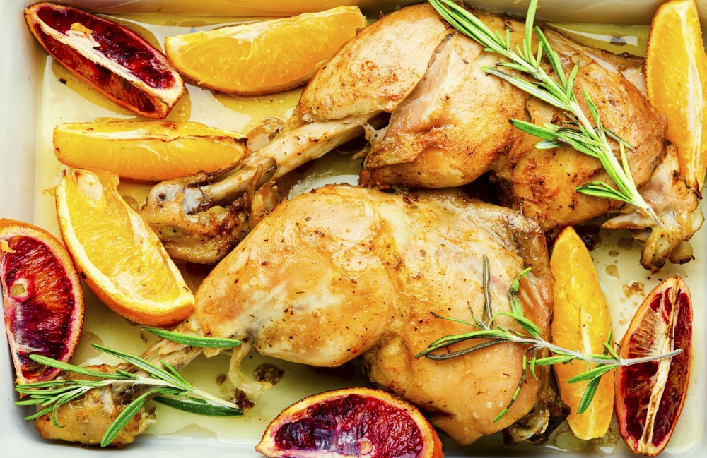 Delicious chicken baked with oranges and rosemary.Food background. Spicy chicken meat roasted with oranges