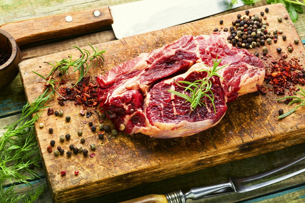 Raw beef meat with rosemary and spices on wooden cutting board. Raw beef meat