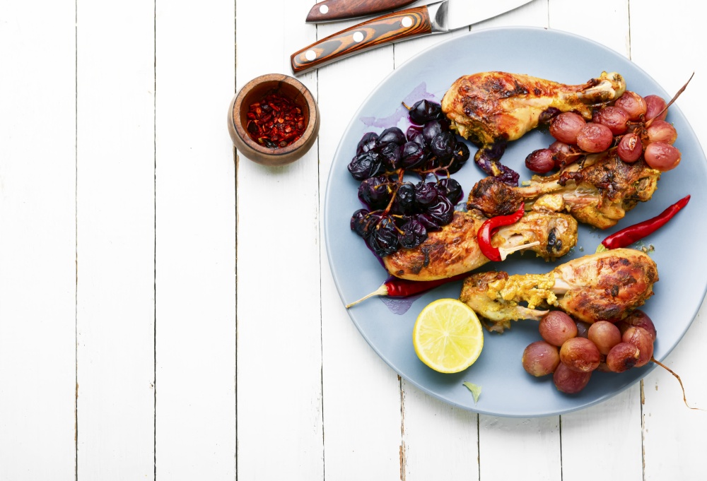 Baked chicken legs with grapes on white wooden background. Barbecued chicken drumsticks