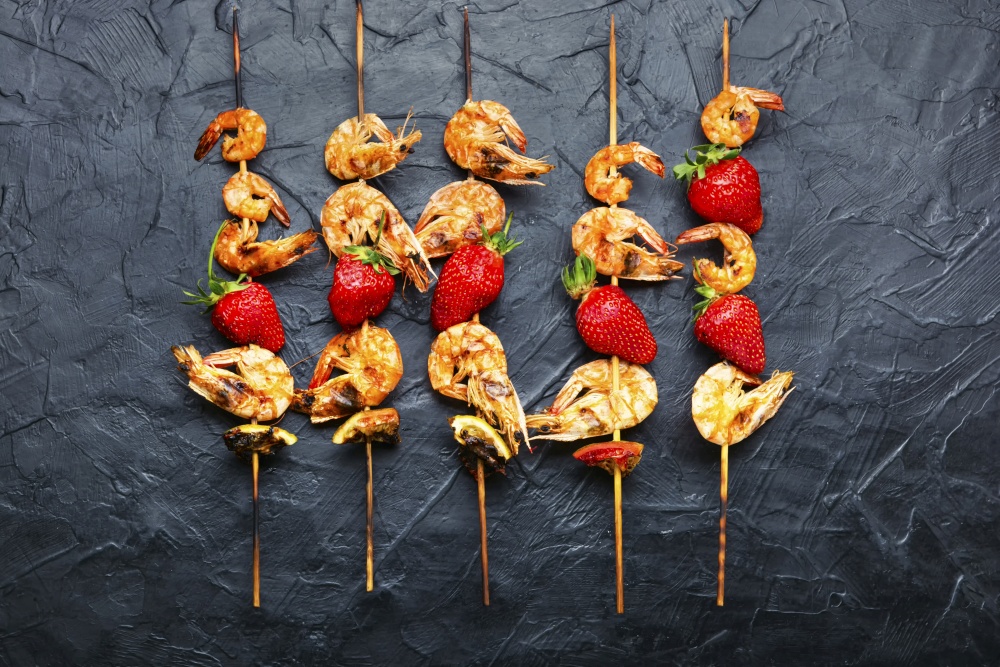 Grilled shrimps on wooden skewers with strawberries.Prawns bbq.Seafood. Grilled tiger shrimps skewers with strawberries