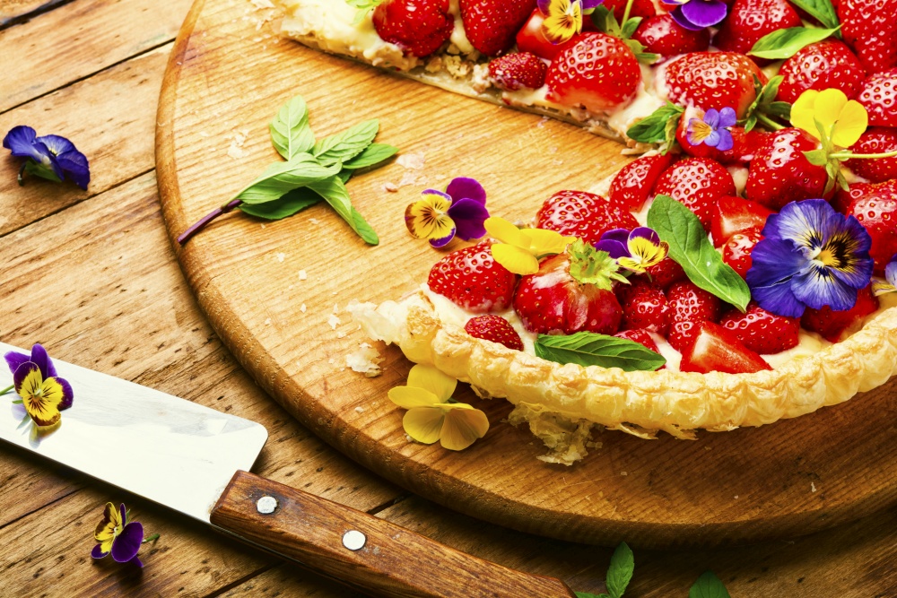 Sliced strawberry pie decorated with edible flowers and mint.Trendy summer berry pie. Open summer pie with strawberry