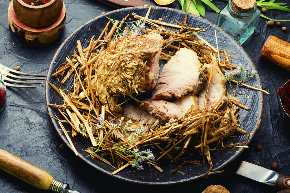 Delicious meat roasted in fresh hay. Baked pork meat in spicy herbs.Autumn food. Roast pork in hay with herbs