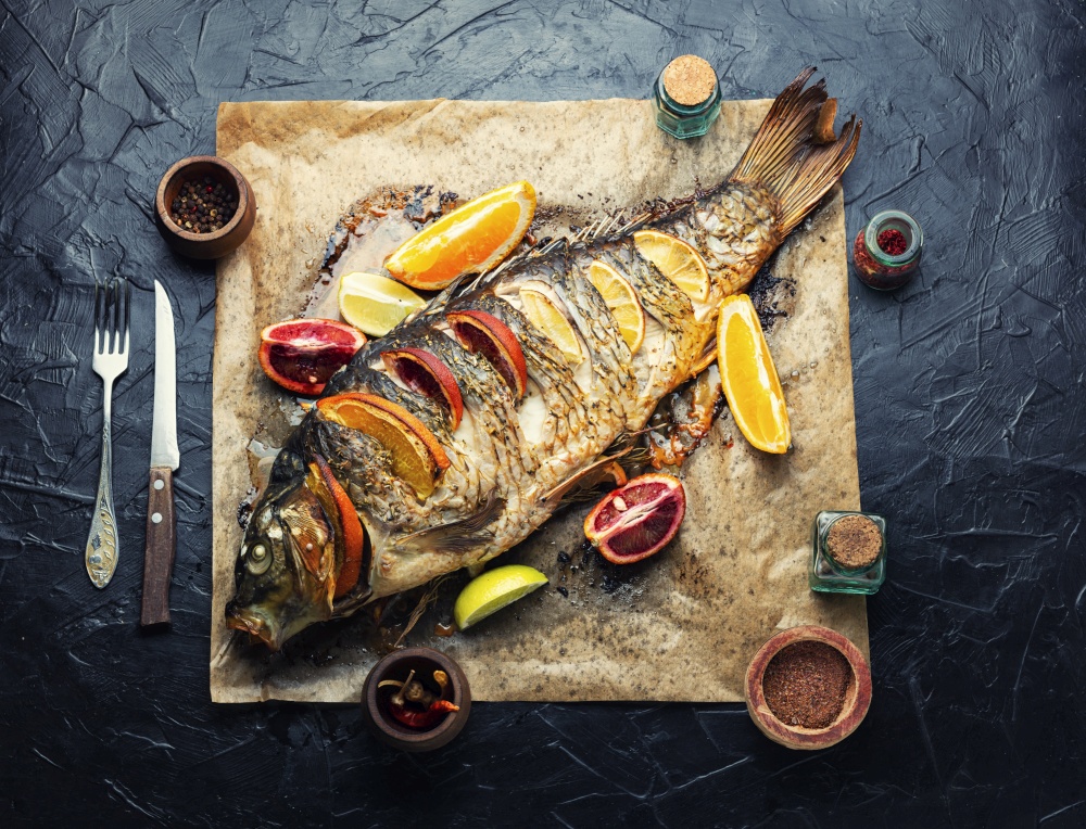 Fish carp grilled whole with lemon and oranges on baking paper. Whole baked carp with citrus fruits.