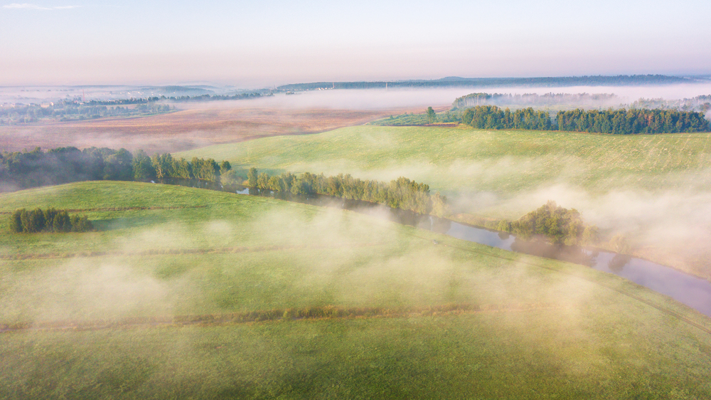 Summer nature landscape aerial panorama. Morning fog over river, meadow and forest. Nature sunlight scene at foggy sunrise. Belarus, Europe