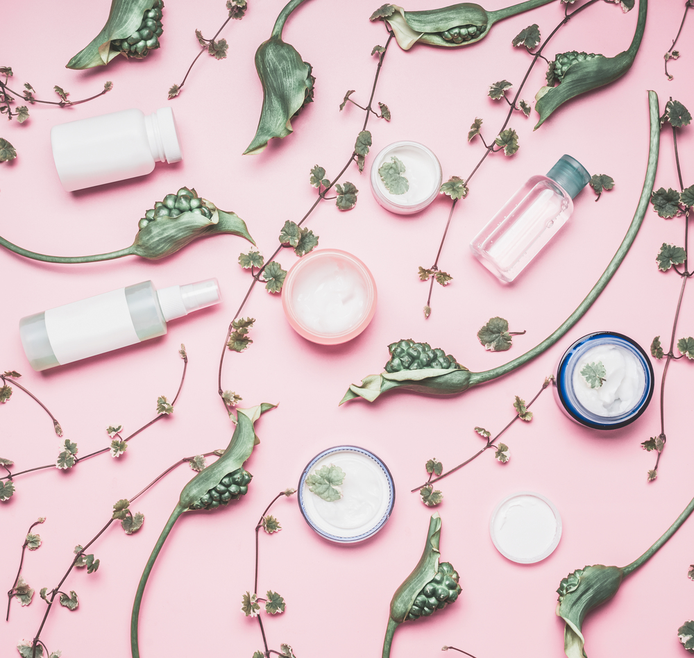 Modern cosmetic flat lay with bottles and facial cream, plants and flowers on pink background. Skin care , beauty and anti-aging concept.  Instagram style.