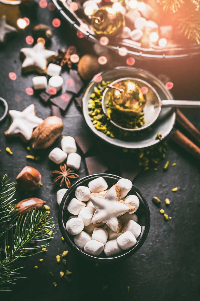 Marshmallow and Christmas star cookies with chocolate and spices: cinnamon, anise and cardamon with nuts on dark background with cozy candle light. Homemade festive sweet gifts preparation.