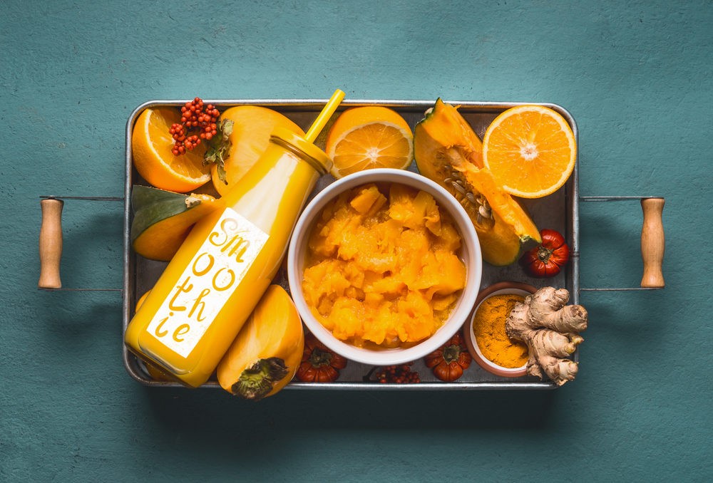 Bottle with healthy energetic drink and word smoothie for cold season with orange ingredients : pumpkin, persimmon , orange fruits, ginger and turmeric or curcuma powder in tray, top view. Clean food