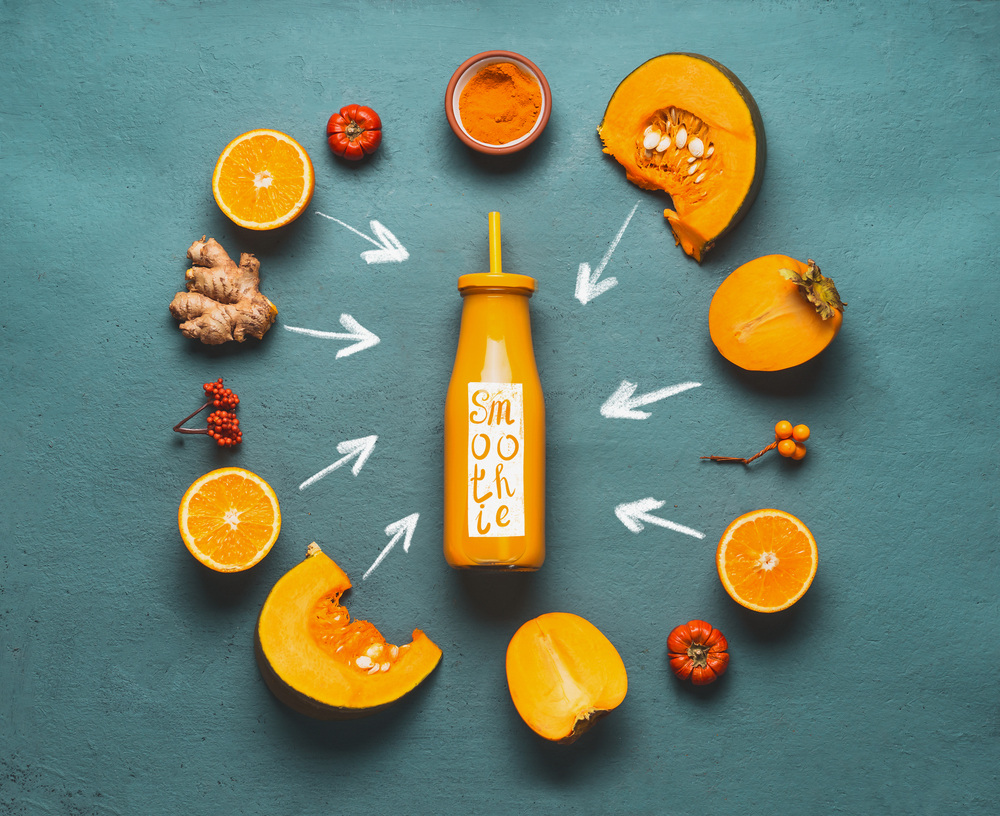 Orange smoothie ingredients : pumpkin, persimmon , orange fruits, ginger and turmeric powder around bottle with healthy energetic drink with word smoothie for cold season , top view.
