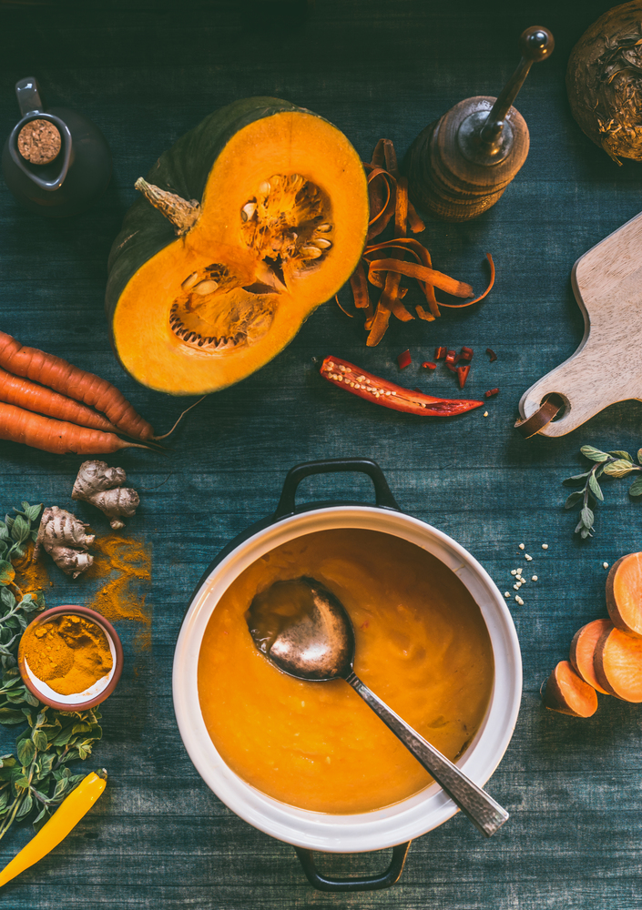 Pumpkin soup. Cooking pot on kitchen table background with orange vegetables and spices ingredients:  with orange cooking ingredients: pumpkin, sweet potato, carrots, turmeric powder,chili and ginger