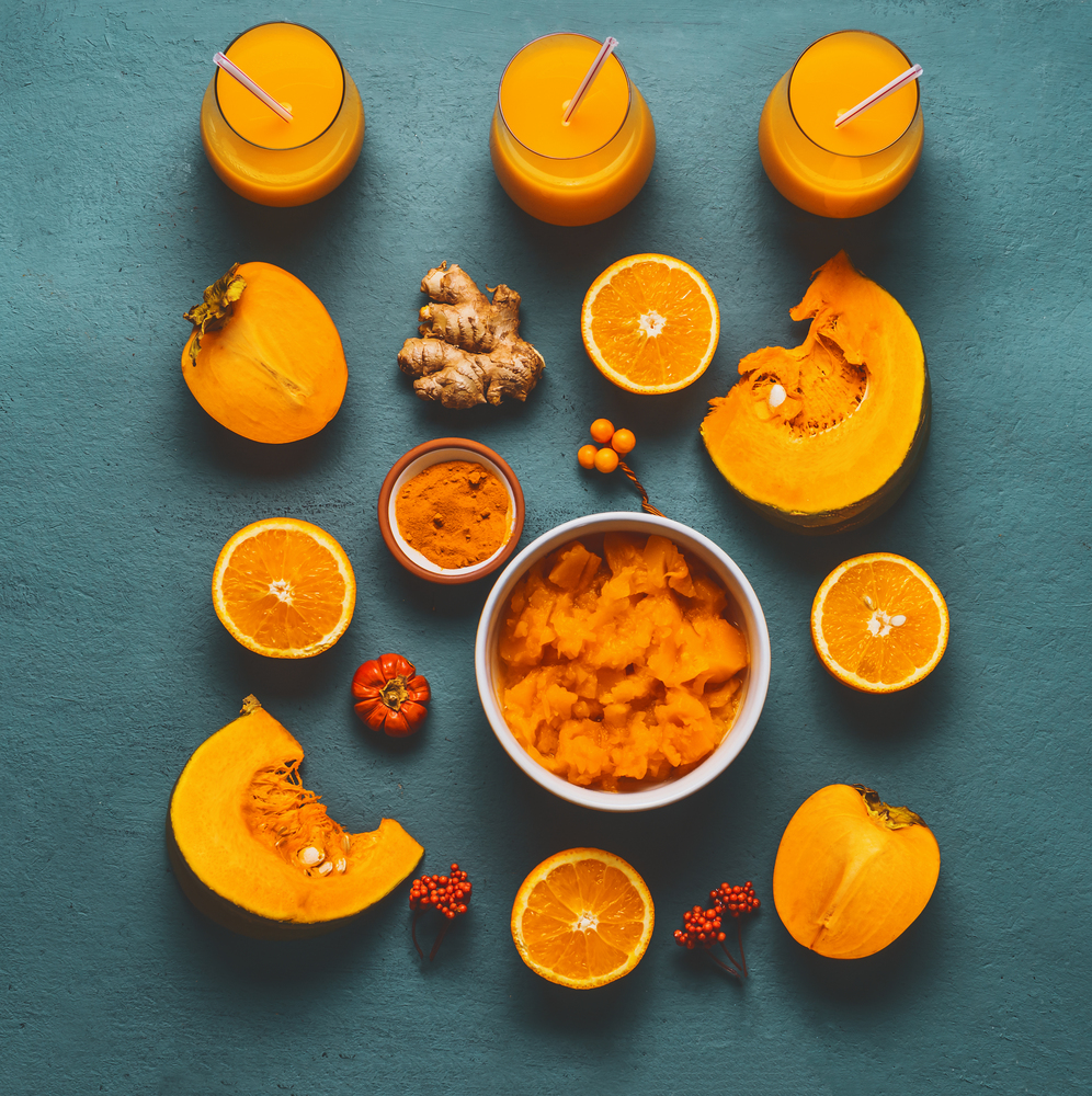 Healthy pumpkin smoothie with orange color ingredients : persimmon , orange fruits, ginger and turmeric powder on blue background, top view, flat lay. Immune boosting beverage for cold season.
