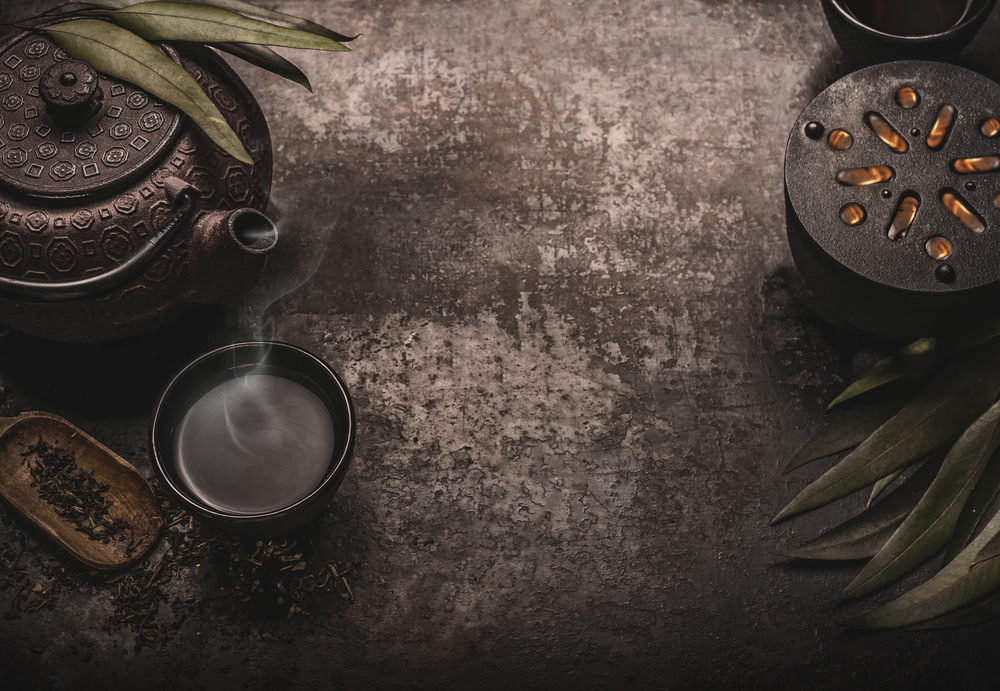 Dark asian tea background with black iron teapot and mug of green tea. Copy space for your design. Authentic vintage style. Traditional tea ceremony arrangement